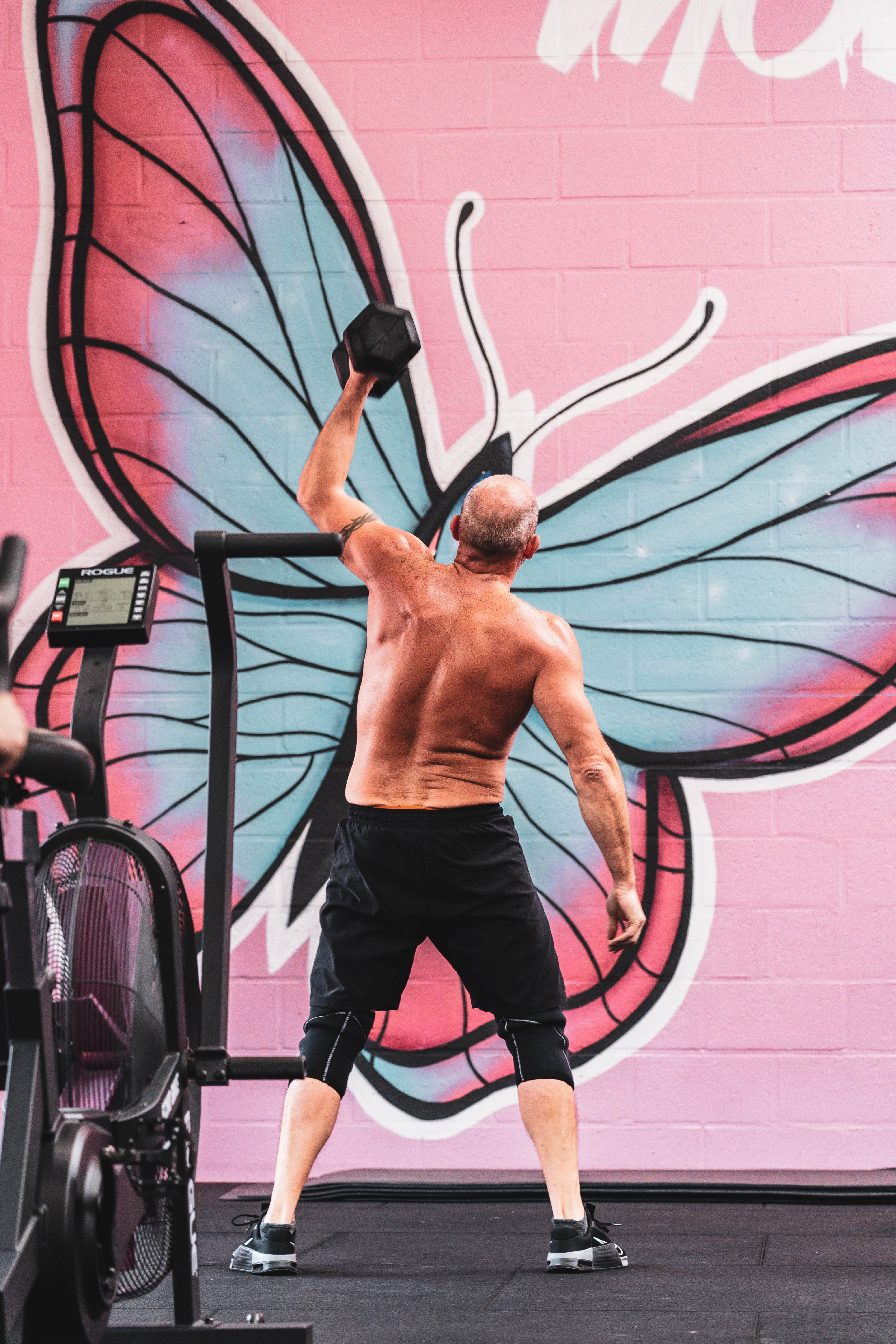 Athlète soulevant un haltère devant une fresque de papillon